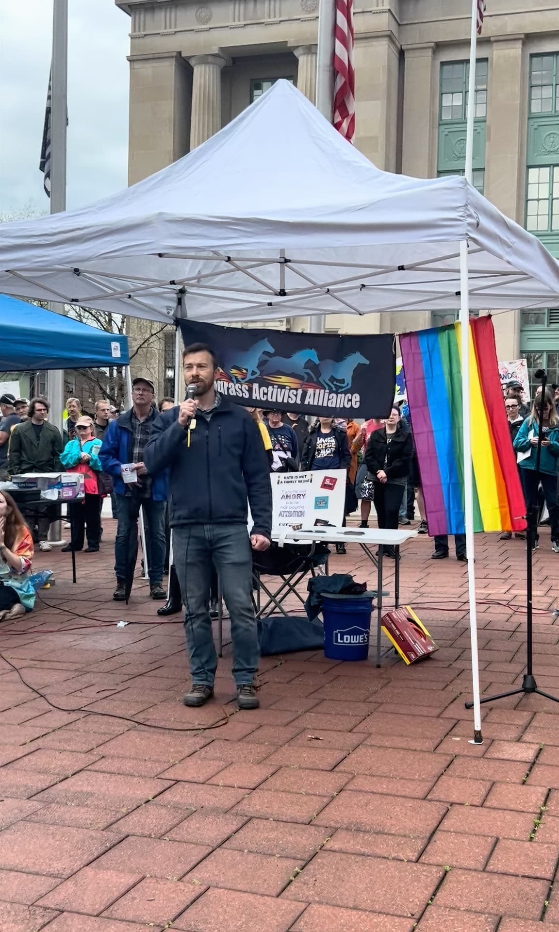 Adam Moore speaking at a Bluegrass Activist Alliance rally with a pride flag
